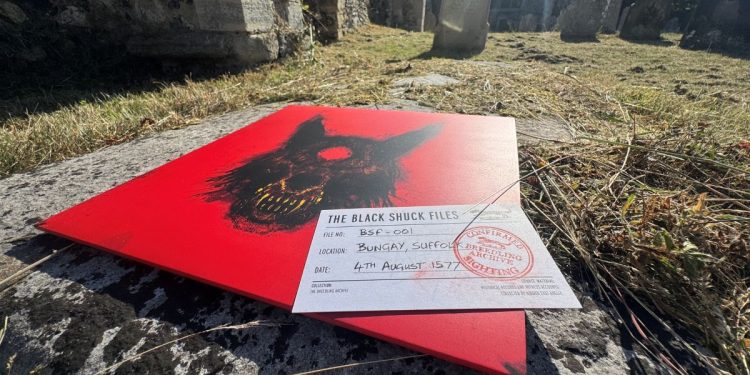 Black Shuck record cover on the ground featuring a menancing black dog against a bright red background