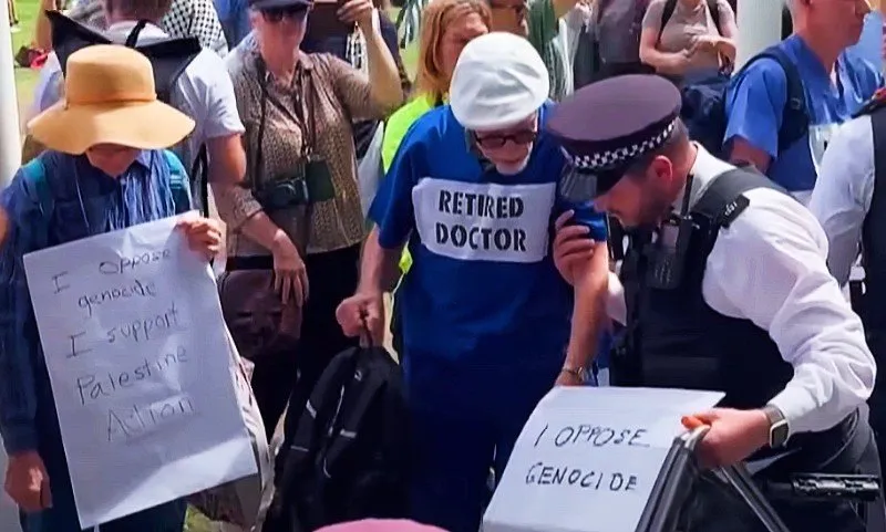 An elderly man wearing a teeshirt that says "retired doctor" is arrested by police