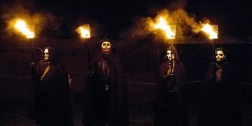 Samhain celebration. Four people in masks and black cloaks hold flaming torches in the darkness