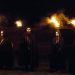 Samhain celebration. Four people in masks and black cloaks hold flaming torches in the darkness