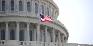 Part of the dome of the white USA Capitol with a single USA flag flying